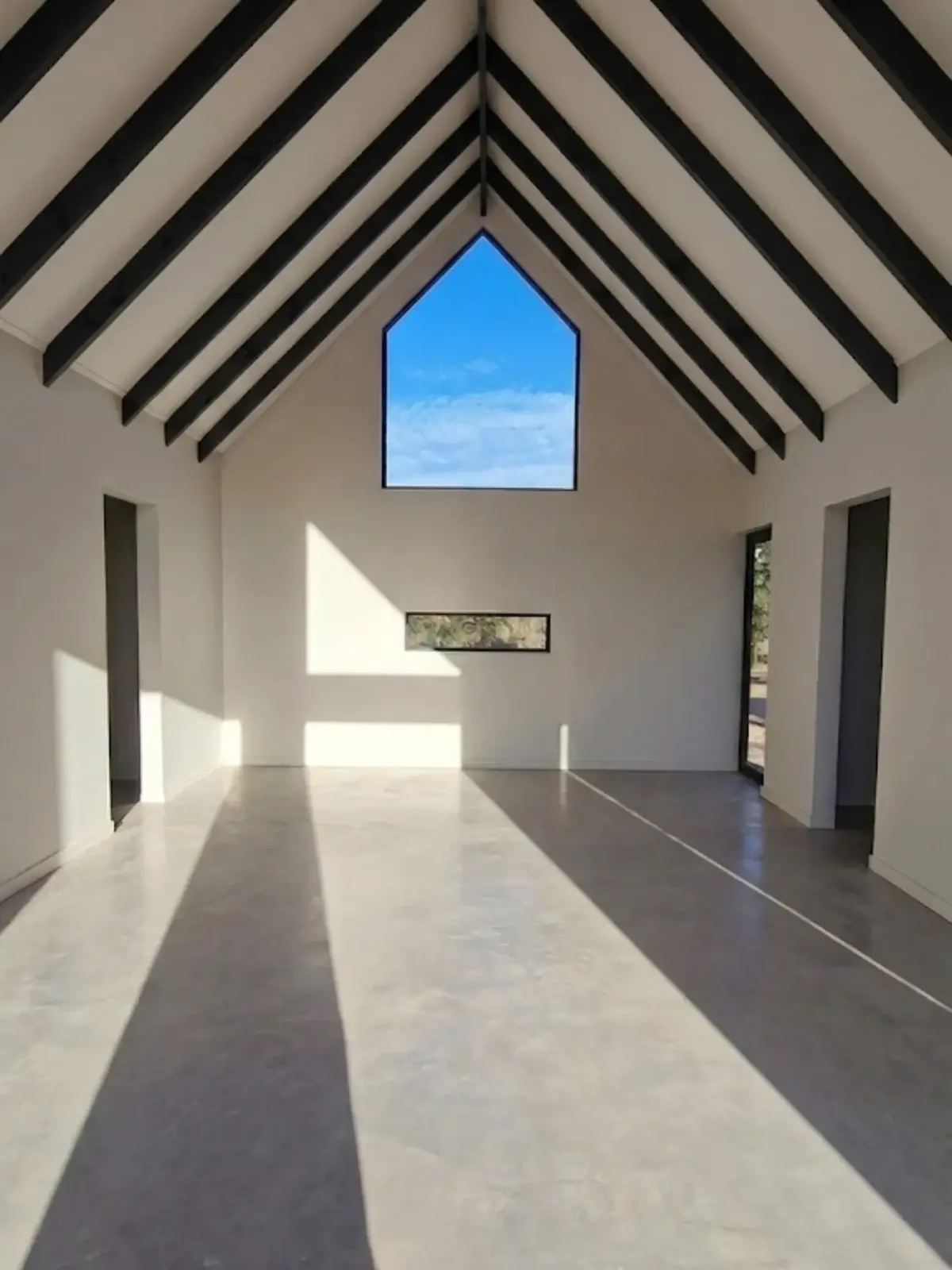 Interior de Nordic Home terminado: muros blancos, vigas negras a la vista y ventana en el frontón