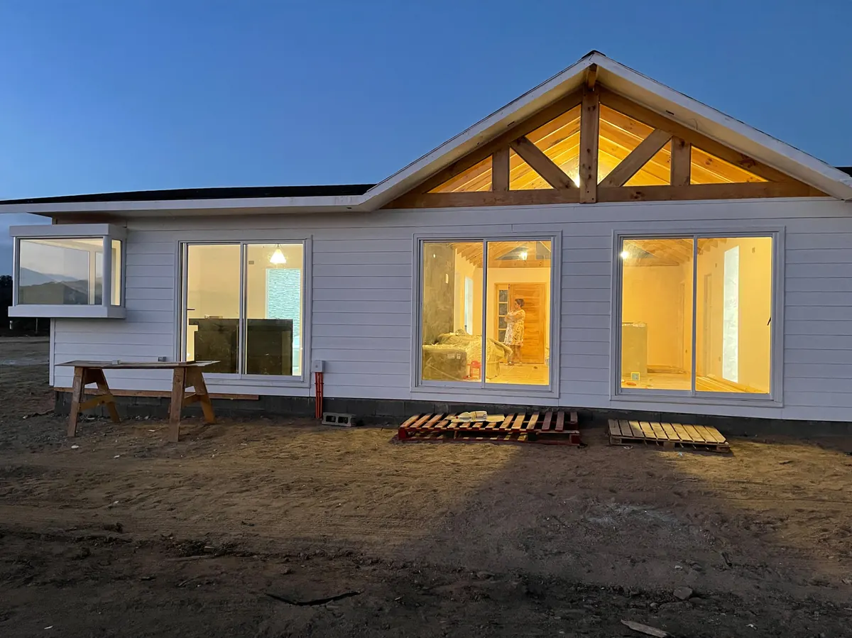 Casa de la Parcela I-5 en La Foresta de Zapallar al atardecer, con frontón de madera iluminado