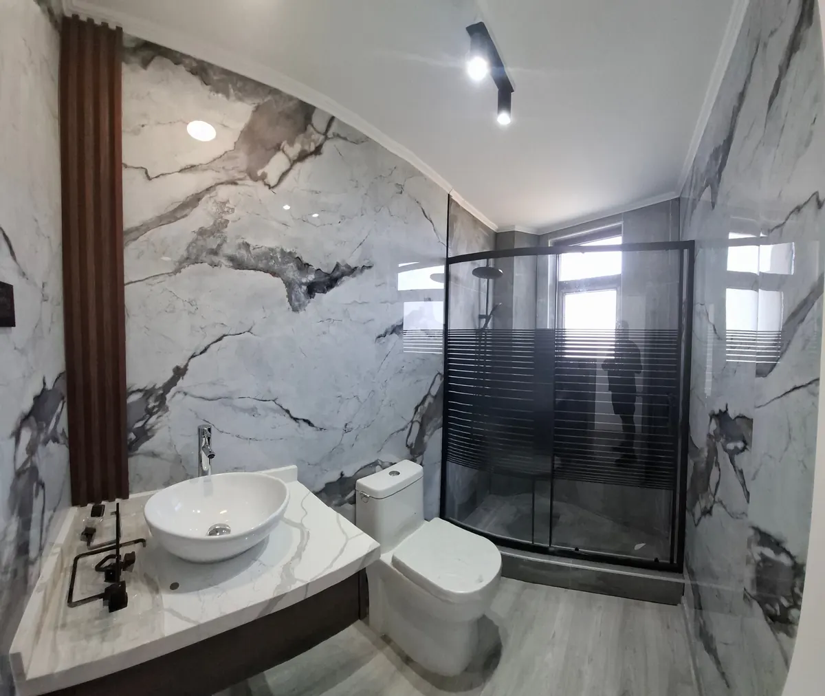 Baño de Casa Mantagua con porcelanato símil mármol, lavamanos de sobreponer y shower door negro