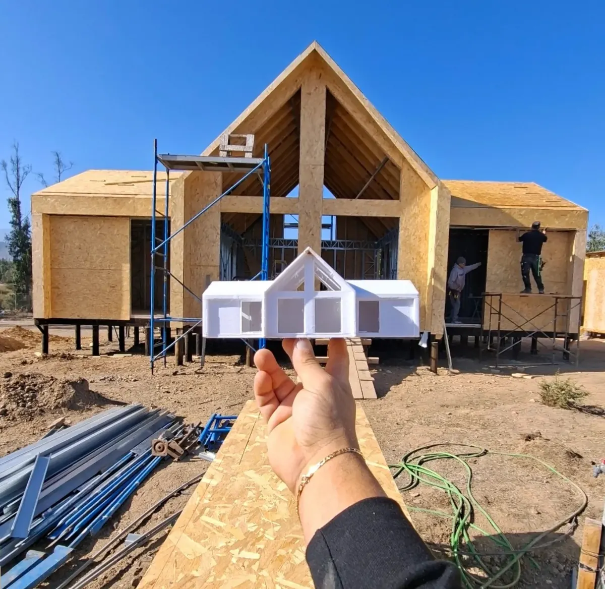 Maqueta de la casa sostenida frente a la misma obra en construcción, La Foresta de Zapallar