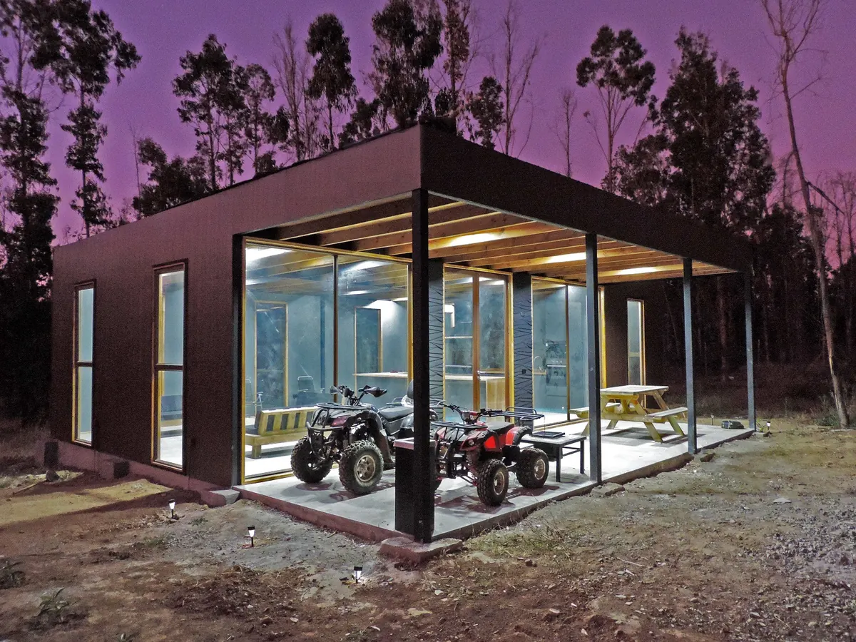 Quincho modular de estructura metálica revestido en madera oscura, iluminado al anochecer