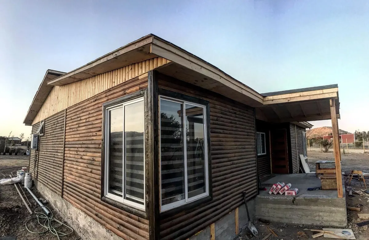Casa V-26 revestida en madera, con ventanas blancas de dos hojas